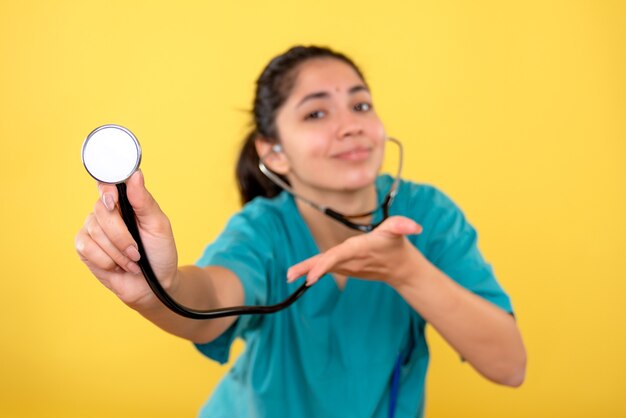 Front view of stethoscope in female hand on yellow isolated wall