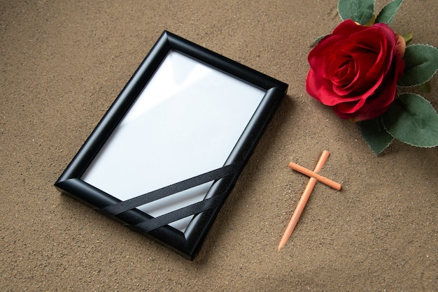 Free photo front view of stick cross with red flower and picture frame on the sand