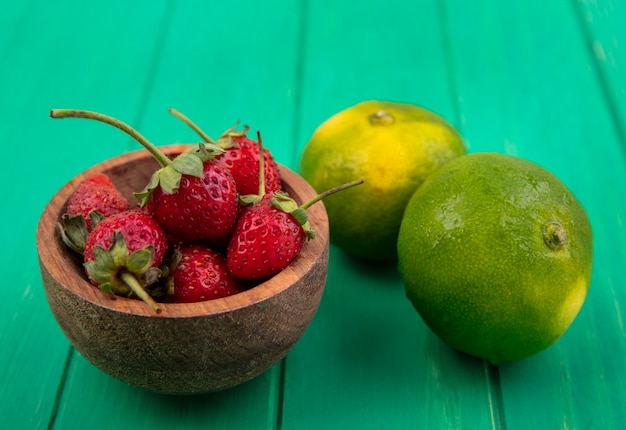 Front view strawberries in a bowl and tangerines on a green wall