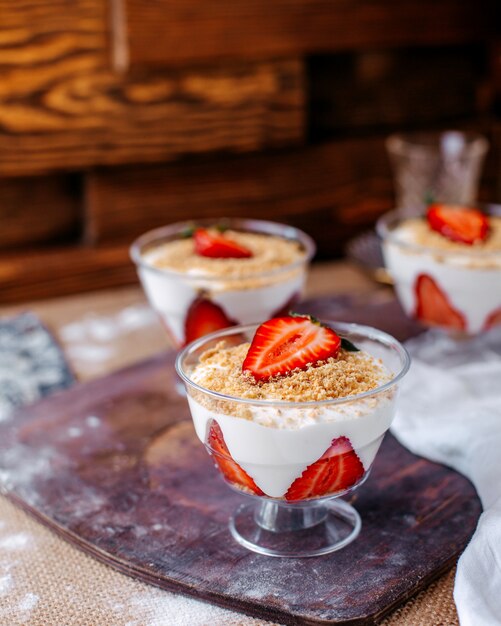 Front view strawberry dessert inside little glasses on the brown surface