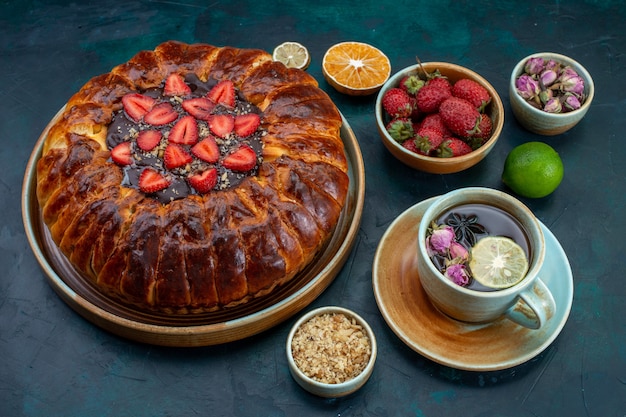 Front view of strawberry pie with cup of tea on dark-blue surface