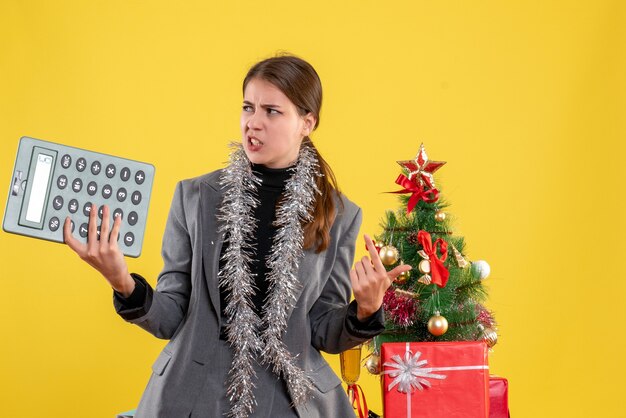 正面図は、クリスマスツリーとギフトカクテルの近くに立っている電卓を持つ女の子を強調しました