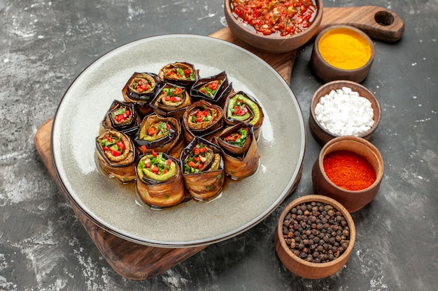 Free photo front view stuffed aubergine rolls in grey oval plate adjika in bowl on wooden cutting board