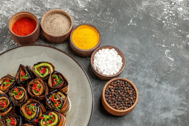 Front view stuffed aubergine rolls hot pepper powder turmeric sea salt black pepper in small bowls on grey background free place