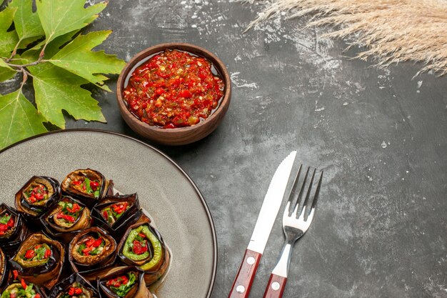 Front view stuffed aubergine rolls on white plate adjika fork and knife on grey with copy space