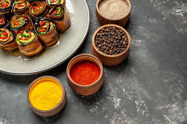 Front view stuffed eggplant rolls on white oval plate salt pepper red pepper turmeric on grey background free place