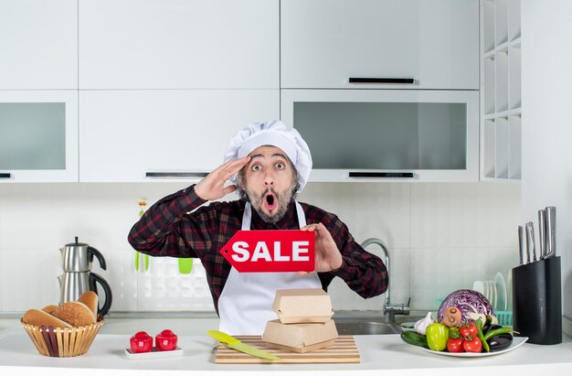 Front view stunned male chef holding up sale sign in the kitchen