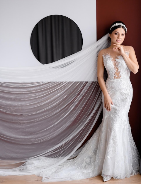 Front view of stunning brunette female model with long veil and accessories on head wearing in seductive and elegant lace mermaid