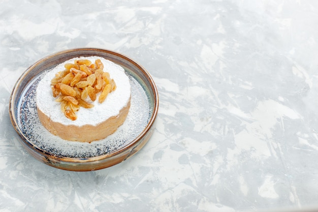 Изюм, сахарная пудра, вид спереди, сушеный виноград на вершине маленького торта внутри тарелки на белом столе изюм фруктовый сахар сладкий торт бисквитный пирог