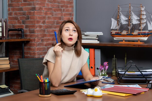 Front view surprised business woman looking up sitting at wall