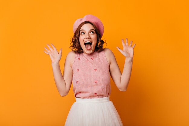 Front view of surprised french girl. Studio shot of amazed elegant woman in beret isolated on yellow background.