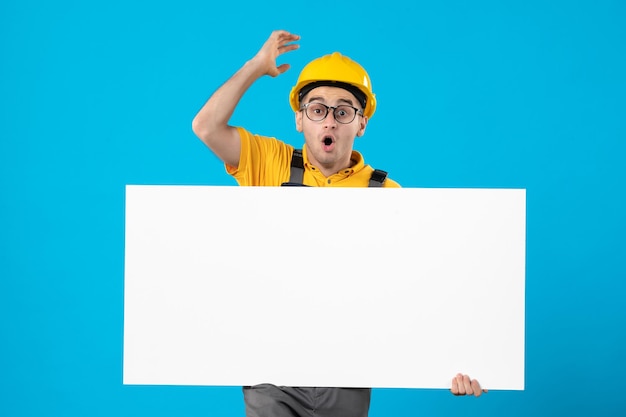 Front view of surprised male builder in yellow uniform with plan blue 