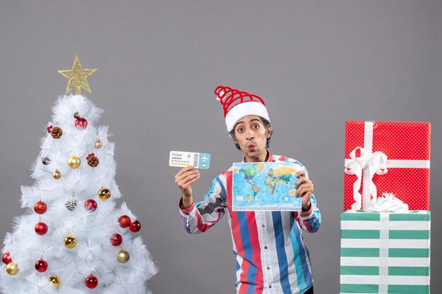 Front view surprised man with spiral spring santa hat holding world map and travel ticket