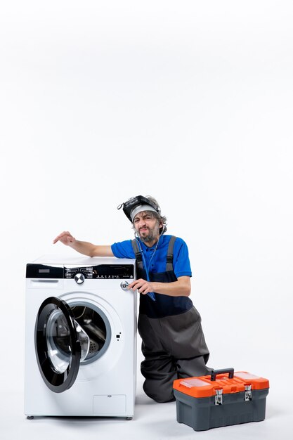 Front view of surprised repairman putting stethoscope on washer tools bag on white wall