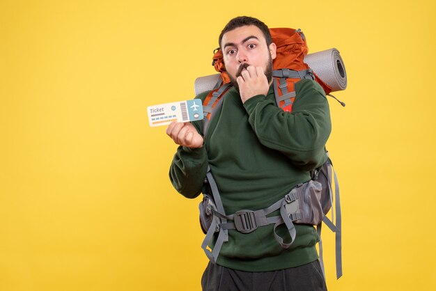 Front view of surprised traveller guy with backpack concentrated on something on yellow background