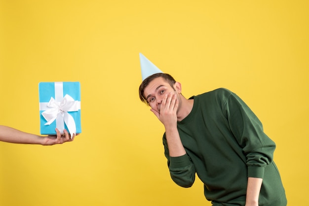 Front view surprised young man gift in human hand on yellow 