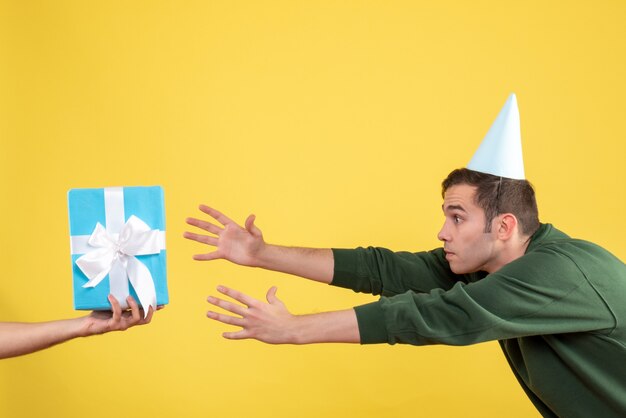 Front view surprised young man trying to catch gift in human hand on yellow 