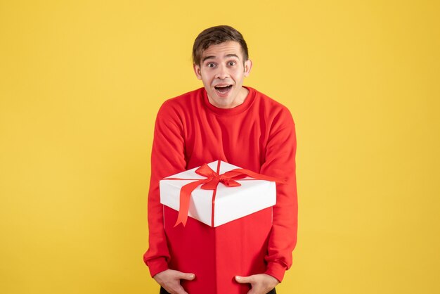 Front view surprised young man with red sweater standing on yellow 