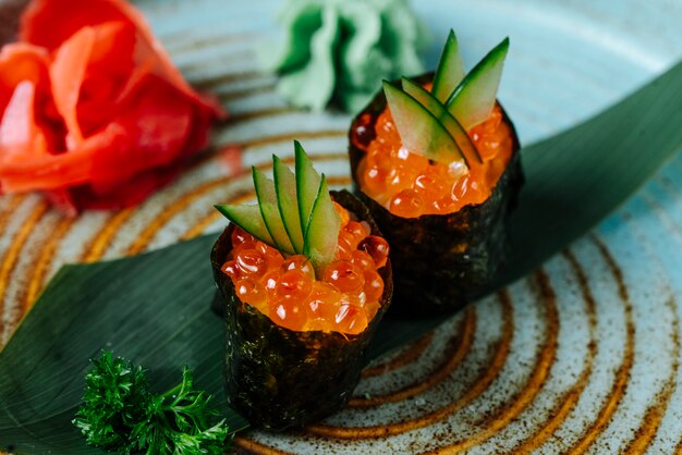 Front view sushi gunkans with red caviar and cucumber with wasabi and ginger on a plate