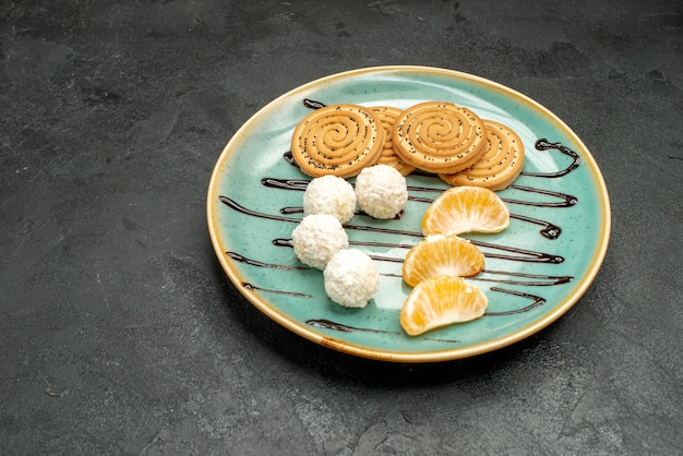 Вид спереди сладкое печенье с кокосовыми конфетами внутри тарелки на темно-сером письменном бисквитном конфетном торте