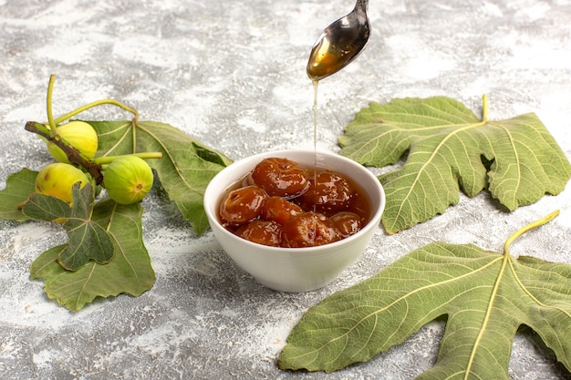 Foto gratuita marmellata di fichi dolci vista frontale con fiori su superficie bianca