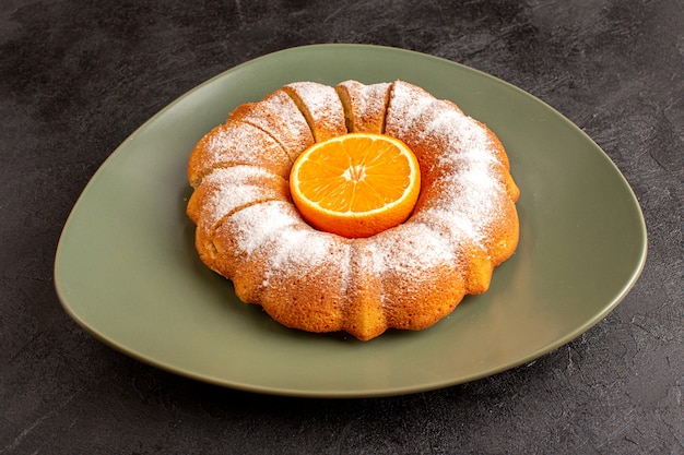 Вид спереди сладкого круглого торта с сахарной пудрой и палочкой апельсина посередине нарезанного сладкого вкусно внутри тарелки и на сером фоне печенья сахарного печенья