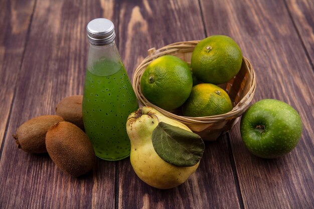 Free photo front view tangerines in a basket with pear kiwi and a bottle of juice on a wooden wall