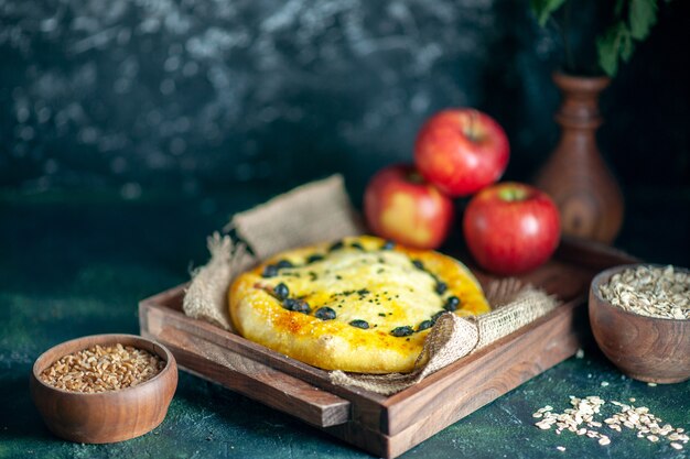 Вид спереди вкусные хлебные яблоки на прямоугольной деревянной доске, овсяные хлопья и зерна пшеницы в мисках на темной поверхности