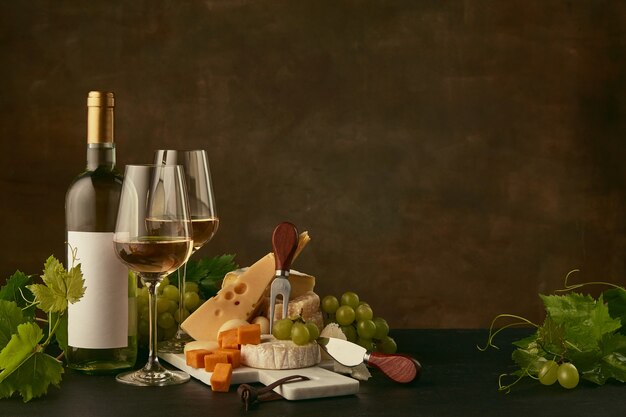 Вид спереди вкусной сырной тарелки с виноградом и бутылкой вина, фруктами и рюмками