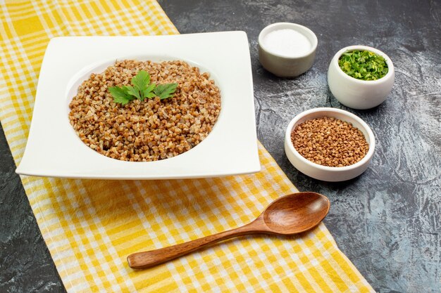 Front view tasty cooked buckwheat inside white plate with greens on light-grey background color dish food photo bean calorie meal