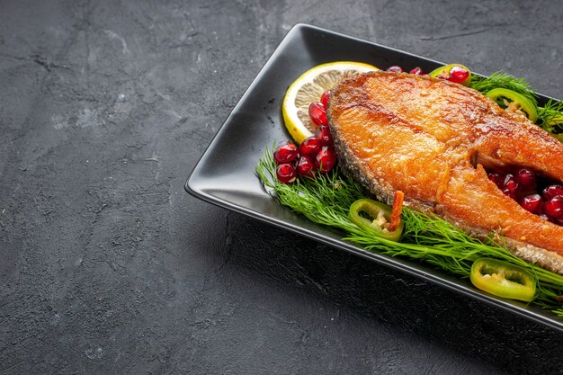 Вид спереди вкусно приготовленная рыба с зеленью и дольками лимона внутри сковороды на темном фоне цвет фрукты морепродукты еда блюдо фото мясо
