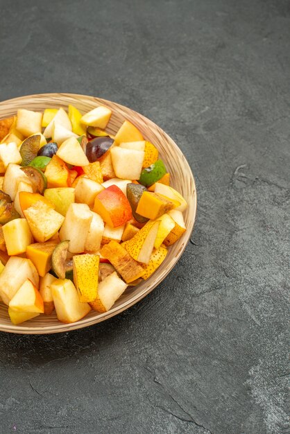 Вид спереди вкусный фруктовый салат состоит из свежих фруктов на сером столе, много свежих фруктов.