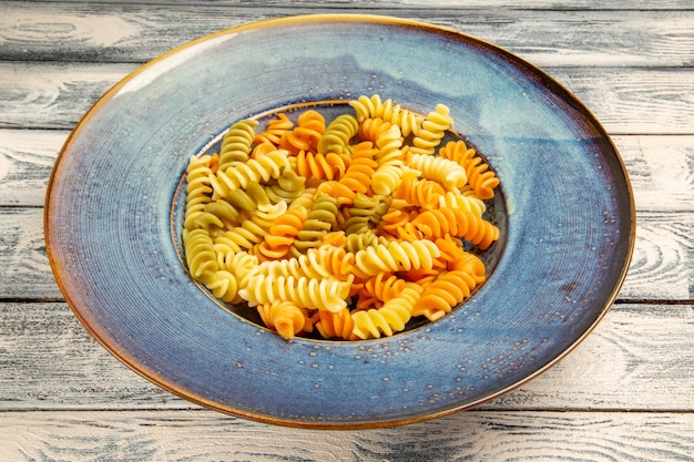 Foto gratuita vista frontale gustosa pasta italiana insolita pasta a spirale cotta su scrivania in legno grigio che cucina cena pasta piatto di pasta