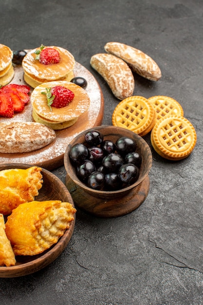 Vista frontale gustose frittelle con diversi dolci su torte di superficie scura zucchero dessert