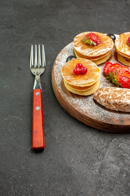 Front view tasty pancakes with sweet cakes and fruits on a dark surface cake dessert sweet