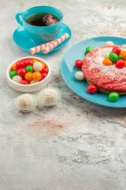 Front view tasty pink cake with candies and cup of tea on white background goodie rainbow candy dessert color cake