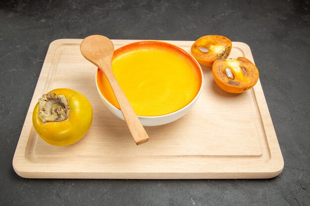 濃いテーブルの皿の色のスープに柿を添えた正面図のおいしいカボチャスープ