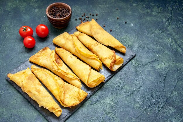 Front view tasty rolled pancakes lined with tomatoes on dark surface