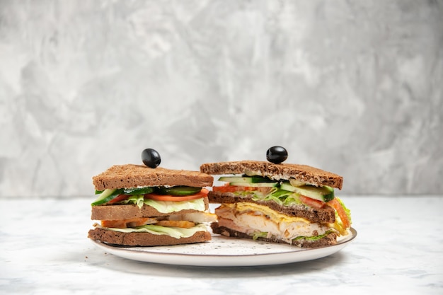 Front view of tasty sandwich with black bread decorated with olive on a plate on stained white surface