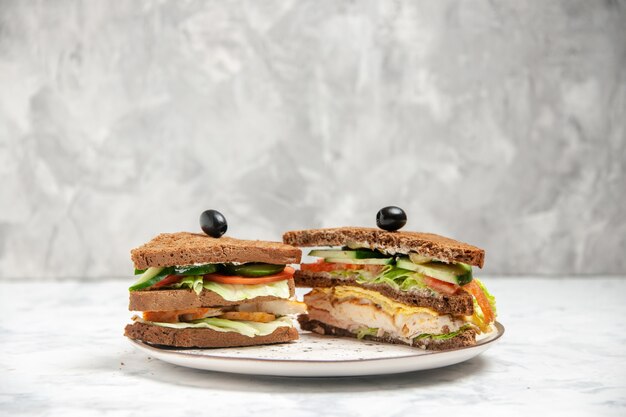 스테인드 흰색 표면에 접시에 올리브로 장식 된 검은 빵과 함께 맛있는 샌드위치의 전면보기
