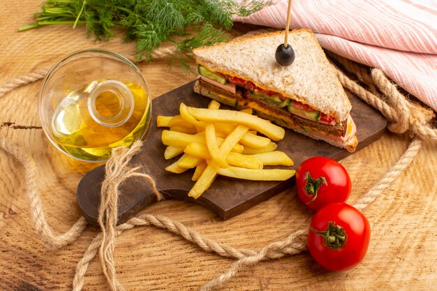 Вкусный бутерброд, вид спереди, с оливковыми помидорами и ветчиной вместе с картофелем фри, масляными помидорами на дереве