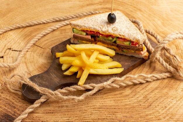 Вкусный бутерброд, вид спереди, с оливковой ветчиной, помидорами, овощами и картофелем фри на дереве