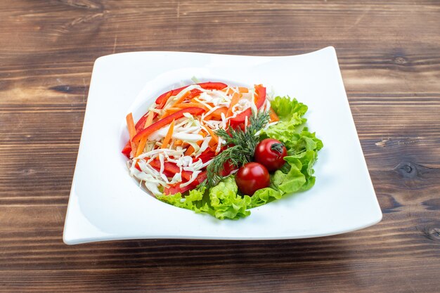 Вид спереди вкусный овощной салат с зеленым салатом и капустой внутри тарелки на коричневой поверхности