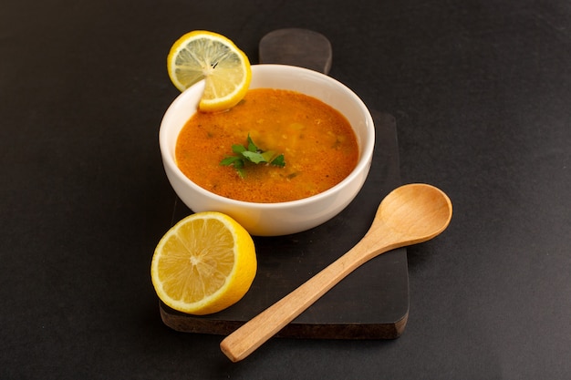 Front view tasty vegetable soup inside plate along with lemon on dark background.