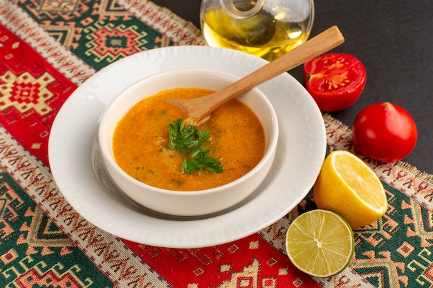 Vista frontale gustosa zuppa di verdure all'interno del piatto con pomodori e limone sulla scrivania scura.
