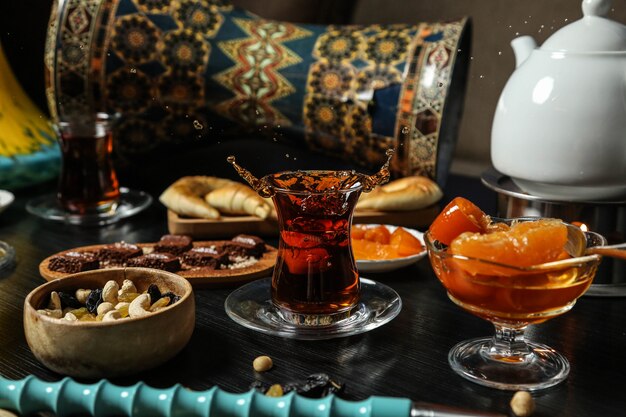 Front view tea set tea in an armudu glass with jam sweets nuts with raisins and a bar of chocolate on the table