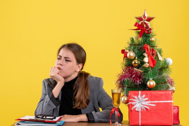 Front view thinking cute girl sitting at the desk xmas tree and gifts cocktail