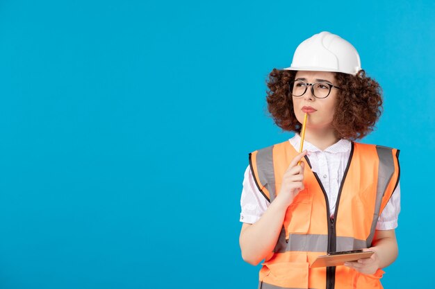 Вид спереди мышления женщина-строитель в форме и шлеме на синей стене