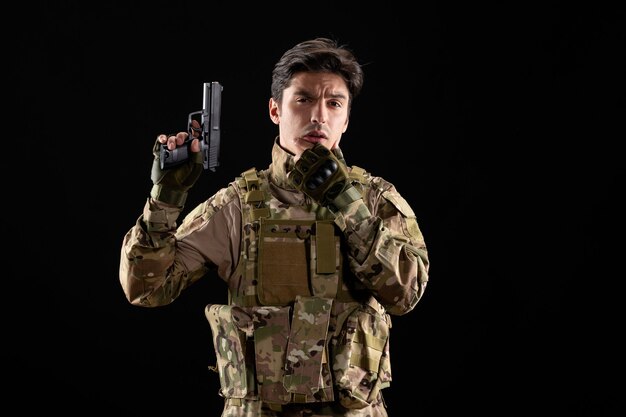 Вид спереди мышления военнослужащего в форме, держащего пистолет на черной стене