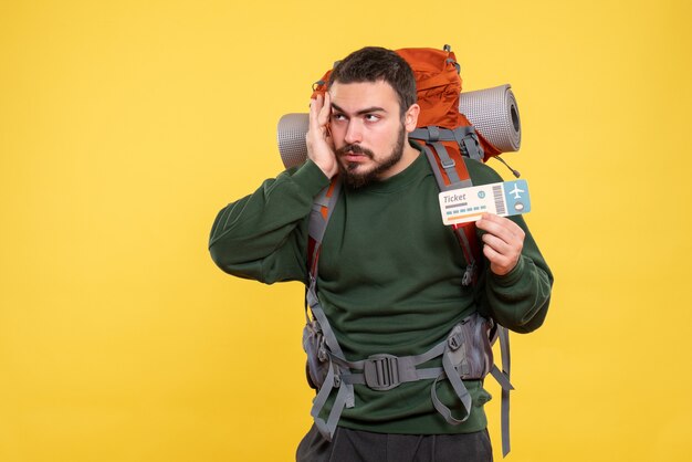 Вид спереди думающего путешествующего парня с рюкзаком и держащего билет на желтом фоне